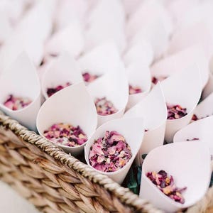 A wicker basket filled with white cone-shaped containers containing pink flower petals.