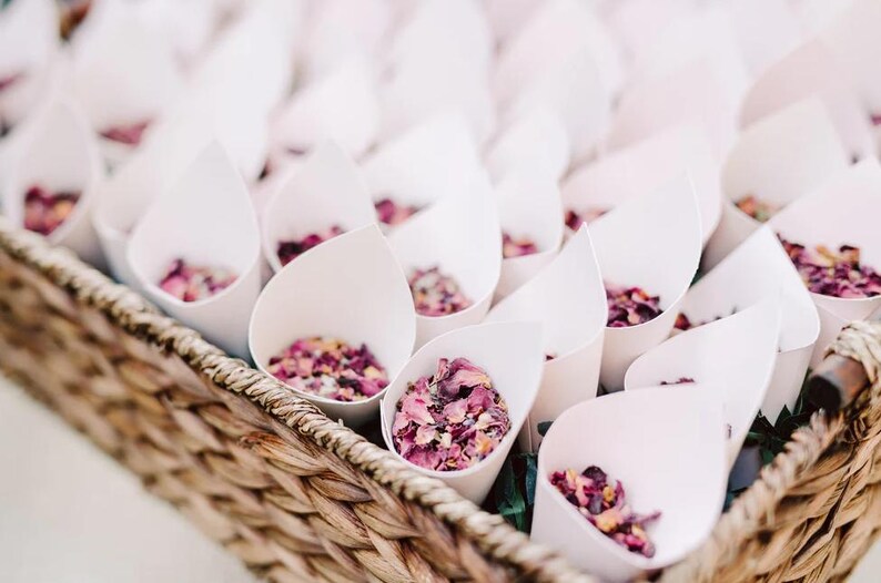 A wicker basket filled with white cone-shaped containers containing pink flower petals.