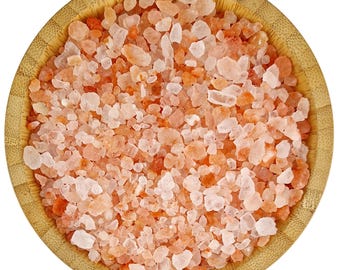 May include: A close-up view of a bowl filled with pink Himalayan salt crystals. The salt crystals are a mix of light pink and white, and they are arranged in a random pattern. The bowl is made of light brown wood.