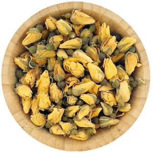 Op de afbeelding: Een houten kom gevuld met gedroogde gele rozenknoppen en groene theebladeren. De rozenknoppen zijn lichtgeel van kleur en de theebladeren zijn donkergroen.