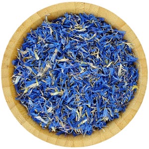 May include: A bowl of dried blue cornflower petals. The petals are a vibrant blue color and are scattered throughout the bowl. The bowl is made of light brown wood.