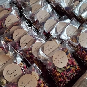a collection of clear plastic bags filled with colorful flower petals, arranged in rows. Each bag has a wooden label with text on it, which appears to be a name or description of the contents inside the bags.