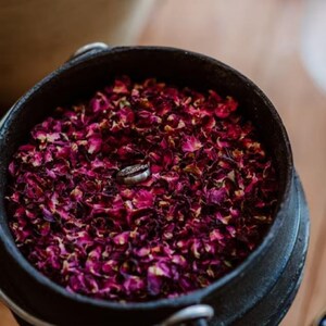 A black pot filled with dried rose petals, with a silver ring resting on top of the petals.