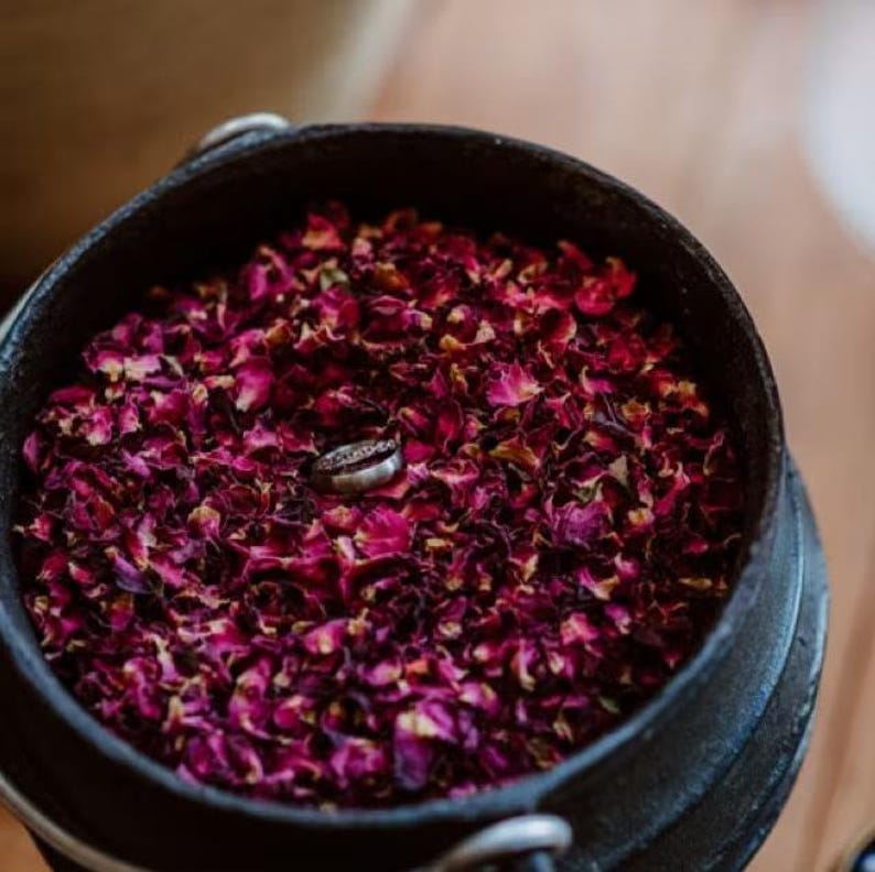 A black pot filled with dried rose petals, with a silver ring resting on top of the petals.