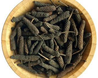 Puede incluir: Un cuenco de madera lleno de granos de pimienta larga secos. Los granos de pimienta son de color marrón oscuro y tienen una textura arrugada.