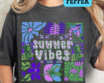 May include: A dark gray t-shirt with a colorful graphic design featuring flowers, leaves, and dragonflies. The text "Summer Vibes" is printed in white with a purple outline.