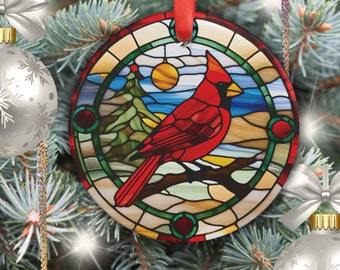 May include: A round glass ornament with a stained glass design of a cardinal bird perched on a branch. The background features a blue sky, a yellow sun, and green trees.