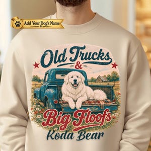 May include: A beige crewneck sweatshirt featuring a graphic of a blue vintage pickup truck with a white Great Pyrenees dog sitting in the truck bed. The text reads Old Trucks & Big Floofs and Koda Bear, with a banner stating Add Your Dog's Name.