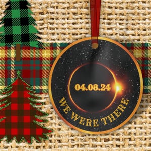 May include: A round, gold-rimmed ornament with a black background and a depiction of a solar eclipse. The date "04.08.24" is printed in yellow on the eclipse. The text "WE WERE THERE" is printed in gold around the eclipse.