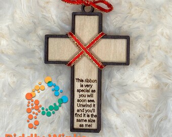 May include: Wooden cross-shaped ornament with a dark brown frame and a light wood center. A red ribbon with gold trim is wrapped around the cross. The text on the cross reads: "This ribbon is very special as you will soon see. Unwind it and you'll find it is the same size as me."