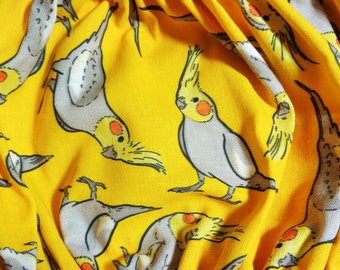 May include: Bright yellow fabric with a repeating pattern of cockatiel birds. The birds are depicted in gray, yellow, and orange, with black outlines. The fabric is gathered, creating folds and shadows.