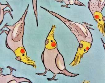 May include: A light blue fabric featuring a repeating pattern of cockatiel birds. The birds are depicted in various poses, with gray bodies, yellow crests, and orange cheek patches. The design is suitable for textiles and crafting projects.