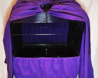 May include: A black birdcage with a purple cover. The cage has a rectangular base and a wire frame. The purple cover drapes over the top and around the base of the cage, creating a dark environment for the bird.