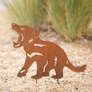 May include: A rusty metal cutout of a Tasmanian devil, standing on two metal spikes, against a background of green grass.