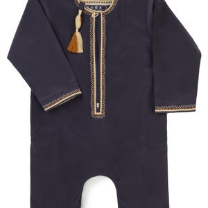 May include: A navy blue baby jumpsuit with long sleeves and a zipper closure. The jumpsuit has a white and brown embroidered trim around the neckline and cuffs. The jumpsuit has a small tassel hanging from the neckline.