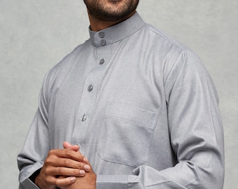 Puede incluir: Una camisa gris de manga larga con cuello abotonado y un solo bolsillo en el pecho izquierdo. La camisa tiene un corte holgado y está hecha de una tela suave y cómoda.