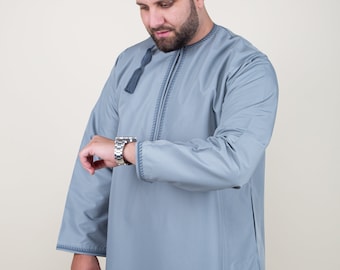 Puede incluir: Un hombre con una camisa de manga larga azul claro con un borla y costuras decorativas. Está mirando su reloj de pulsera.