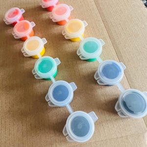 May include: A set of 10 paint pots with lids, arranged in two rows. The paint colours are red, orange, yellow, green, blue, and black.