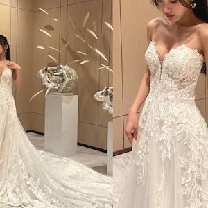 Op de afbeelding: Een witte strapless bruidsjurk met een sweetheart-halslijn en ingewikkelde kantdetails. De jurk heeft een vloeiende A-lijn silhouet en een lange sleep.