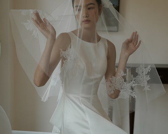 May include: A white bridal veil with delicate lace detailing. The veil is made of soft tulle and has a scalloped edge.