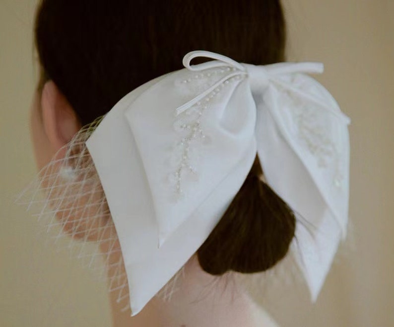 May include: A white satin bow with pearl embellishments and a delicate tulle veil. The bow is tied in a large, elegant knot and is perfect for adding a touch of sophistication to any hairstyle.