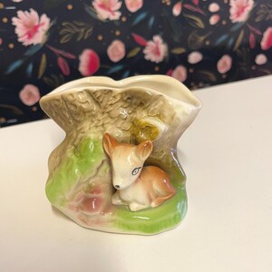 May include: A ceramic planter shaped like a tree stump with a fawn peeking out from behind the trunk. The planter is painted in shades of brown, green, and pink.