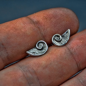 Peut inclure: Une paire de boucles d'oreilles en argent avec un motif en spirale. Les boucles d'oreilles sont petites et délicates, et elles ont une finition texturée.