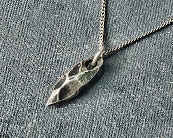 May include: A silver necklace with a textured, pointed pendant. The pendant is shaped like a leaf or a teardrop.