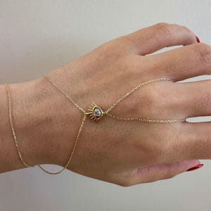 May include: A gold chain bracelet with an eye charm featuring a clear gemstone. The bracelet is designed to wrap around the wrist and finger.