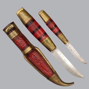 Könnte beinhalten: Zwei Messer mit Metallklingen und rot-schwarzen Griffen mit Messingakzenten. Das größere Messer hat eine rote Scheide mit Messingverzierungen. Die Klingen sind mit den Texten O. Tammio Made in Finland und J. Marttiini Made in Finland graviert.