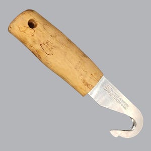 Op de afbeelding: Een Mora roestvrijstalen haakmes met een lichtgekleurd, getextureerd houten handvat met een rond gat aan de bovenkant. Het metalen lemmet is in een haakvorm gebogen en gegraveerd met de tekst Mora, Made in Sweden en Stainless Steel.
