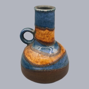 May include: A ceramic vase with a blue, brown, and orange color scheme. The vase has a rounded body, a cylindrical neck, and a small handle. The design features horizontal bands of color and a dark brown base.