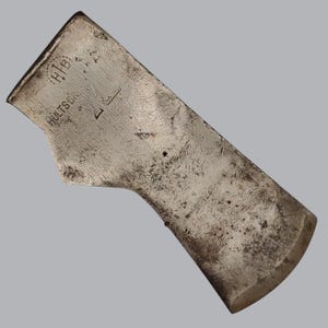 Peut inclure: Une tête de hache en acier patiné avec une finition argentée métallique et une texture de surface visible. Le métal est estampillé avec le texte HULTS BRUK et les lettres HIB dans un contour circulaire. La tête de hache a un tranchant incurvé.