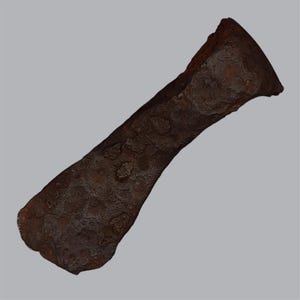 May include: A weathered, dark brown iron axe head with a heavily pitted and oxidized surface texture. The tool features a wide, curved cutting edge that tapers toward a narrower, flared poll, showing significant signs of age and heavy corrosion.