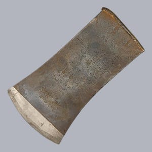 Peut inclure: Gros plan d'une tête de hache vintage avec une surface usée et texturée. La tête de hache est principalement de couleur métal sombre et vieilli avec un tranchant argenté. Le texte "SANDVIK SWEDEN" est visible.