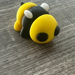 May include: A 3D printed bumble bee toy with black and yellow stripes, white wings, and black eyes.