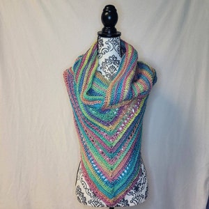 May include: A colorful crocheted shawl with a rainbow pattern in shades of pink, green, blue, and yellow. The shawl is draped over a mannequin.