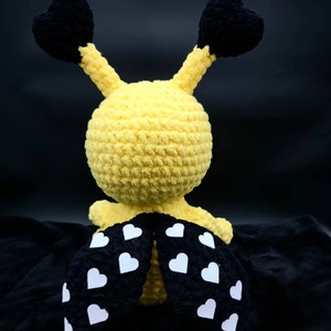 May include: A crocheted yellow bee toy with black heart-shaped wings and white heart-shaped spots on its black legs.