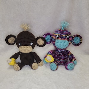 May include: Two crocheted monkey toys. One is brown with a yellow banana and the other is purple, blue, and pink with a yellow banana.