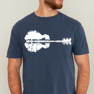 May include: A navy blue t-shirt with a white graphic of a guitar silhouette made of trees reflected in water.
