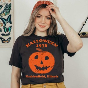 May include: A black t-shirt with a vintage-style graphic of a jack-o'-lantern with the text "Halloween 1978 Haddonfield, Illinois".