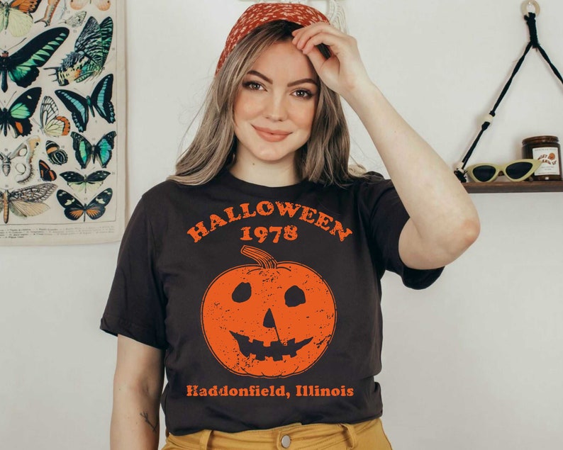 May include: A black t-shirt with a vintage-style graphic of a jack-o'-lantern with the text "Halloween 1978 Haddonfield, Illinois".