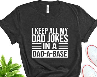 May include: A dark gray t-shirt with the text "I keep all my dad jokes in a dad-a-base" printed in white.