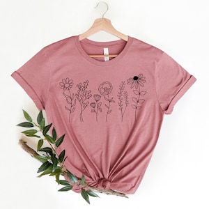 May include: A mauve t-shirt with a black line drawing of a row of flowers on the front.