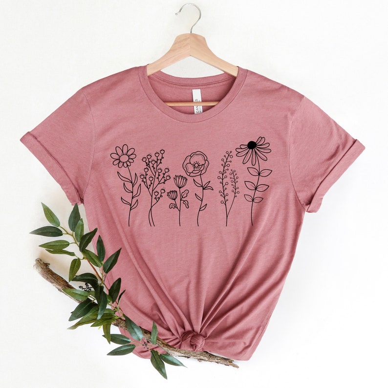 May include: A mauve t-shirt with a black line drawing of a row of flowers on the front.