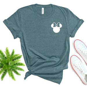 May include: A teal blue t-shirt with a white silhouette of Minnie Mouse's head with a bow on top.