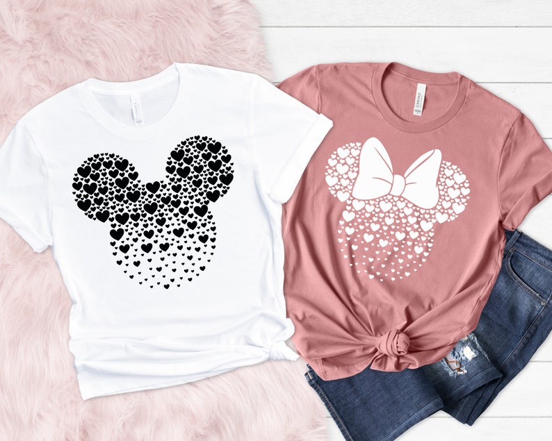 Może przedstawiać: Dwie koszulki z sercowatym wzorem Mickey Mouse'a i Minnie Mouse. Koszulka Mickey Mouse'a jest biała z czarnymi sercami, a koszulka Minnie Mouse'a jest r&oacute;żowa z białymi sercami.