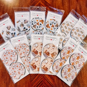 May include: A collection of 10 round car coasters featuring various Disney characters. The coasters are white with colorful designs. The coasters are packaged in clear plastic bags with the text "Car Coasters" and "Handmade with love".