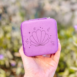 May include: A small purple velvet jewelry box with a seashell design and a zipper closure.