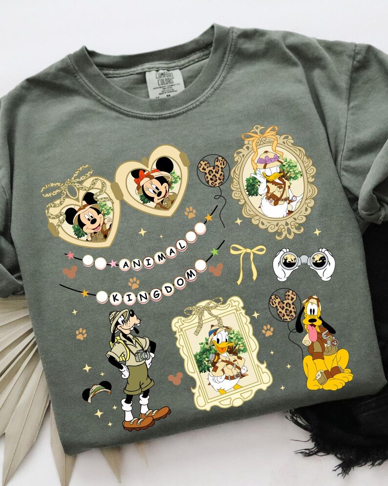 May include: A green t-shirt with a print of various Disney characters in an animal kingdom theme. The characters include Mickey Mouse, Minnie Mouse, Donald Duck, Goofy, and Pluto. The text "Animal Kingdom" is printed on the shirt.